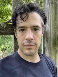 a man in a black shirt standing in front of a wooden fence